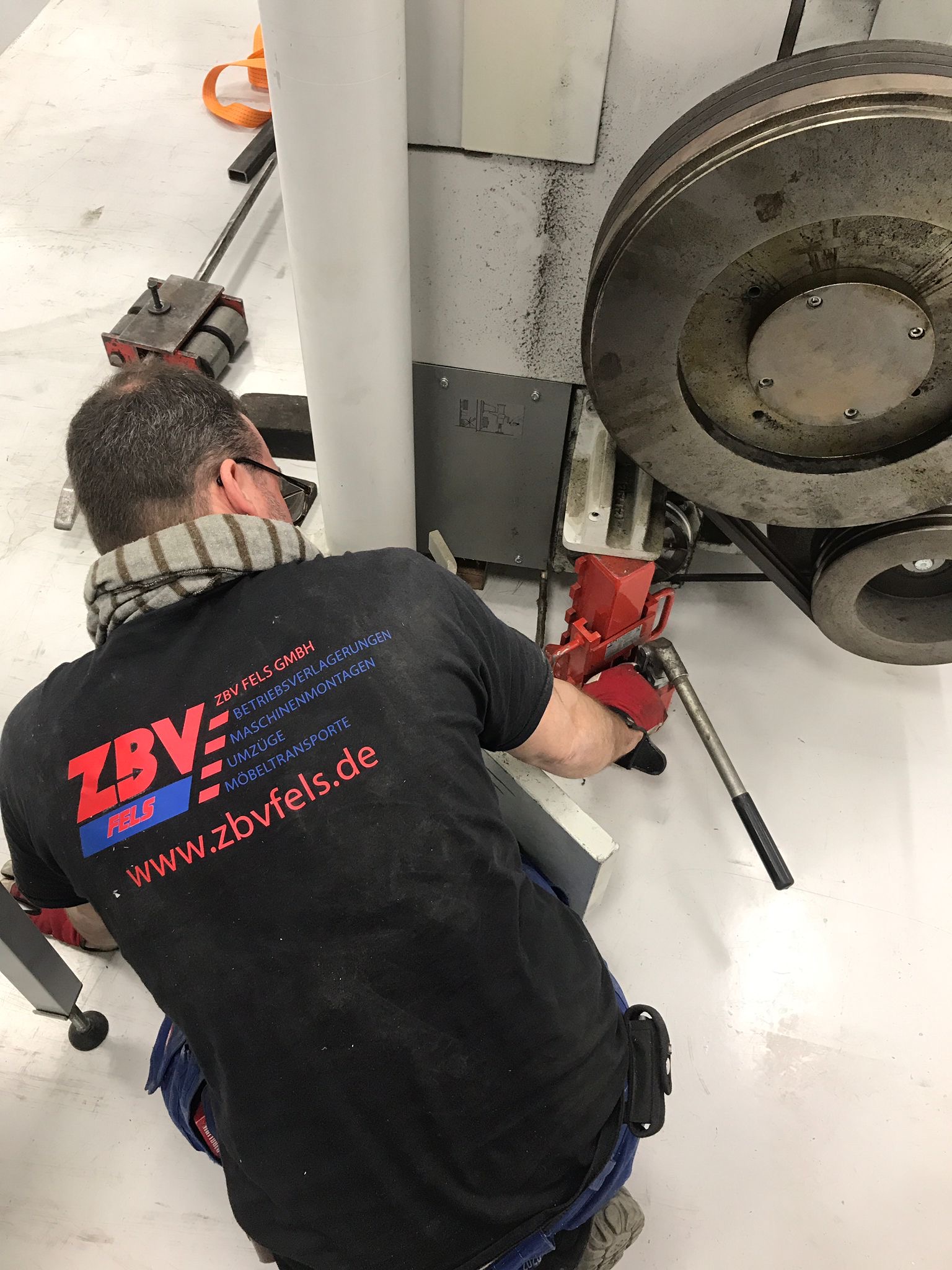 Mann mit schwarzem T-Shirt und Maske arbeitet an einer Maschine in Werkstatt.