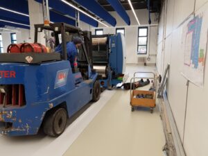 A forklift in a workshop with two people working on a machine.
