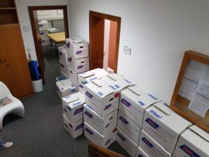 Several stacked moving boxes in an office hallway with doors and furniture.