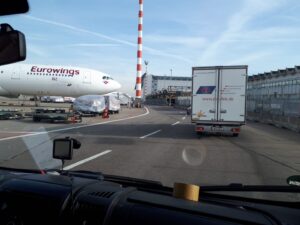A view from a vehicle of an airport with a parked Eurowings plane and a truck on the road.