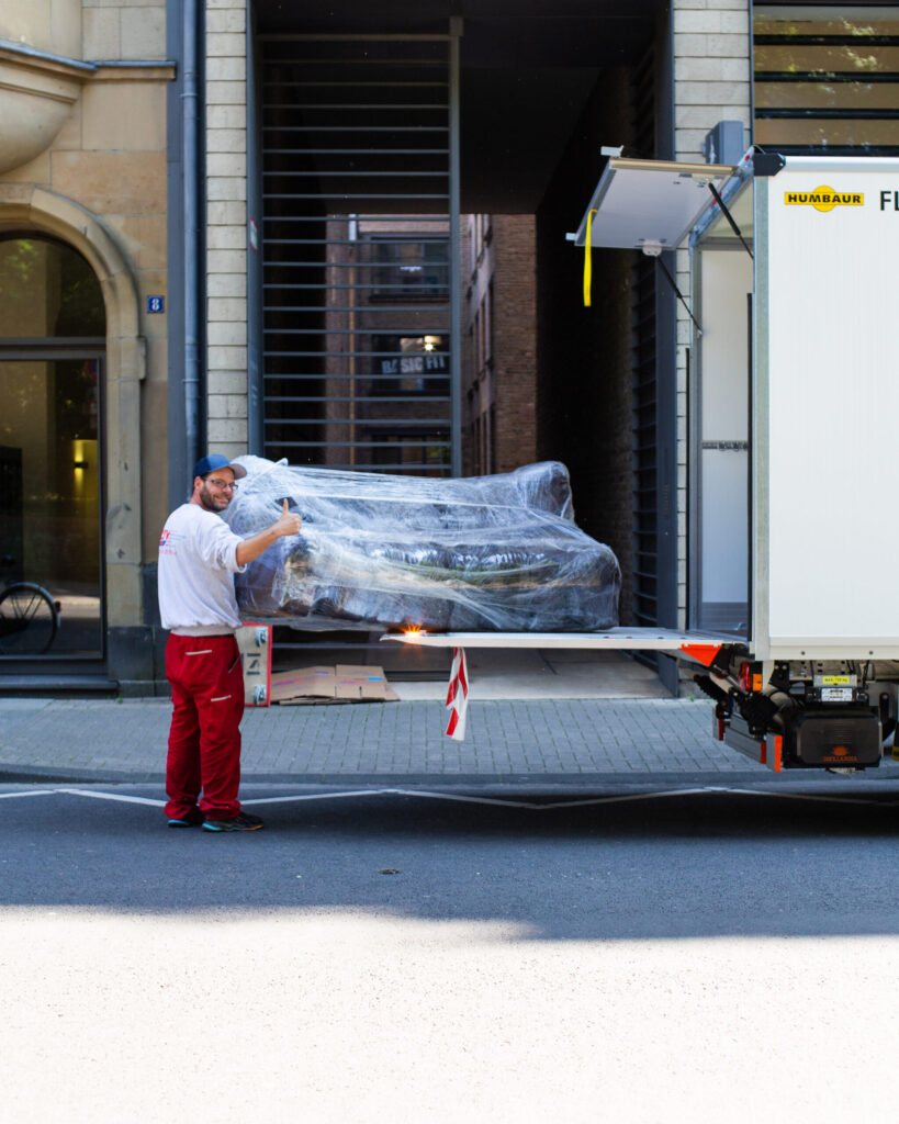 An employee is holding a wrapped sofa on a truck loading dock