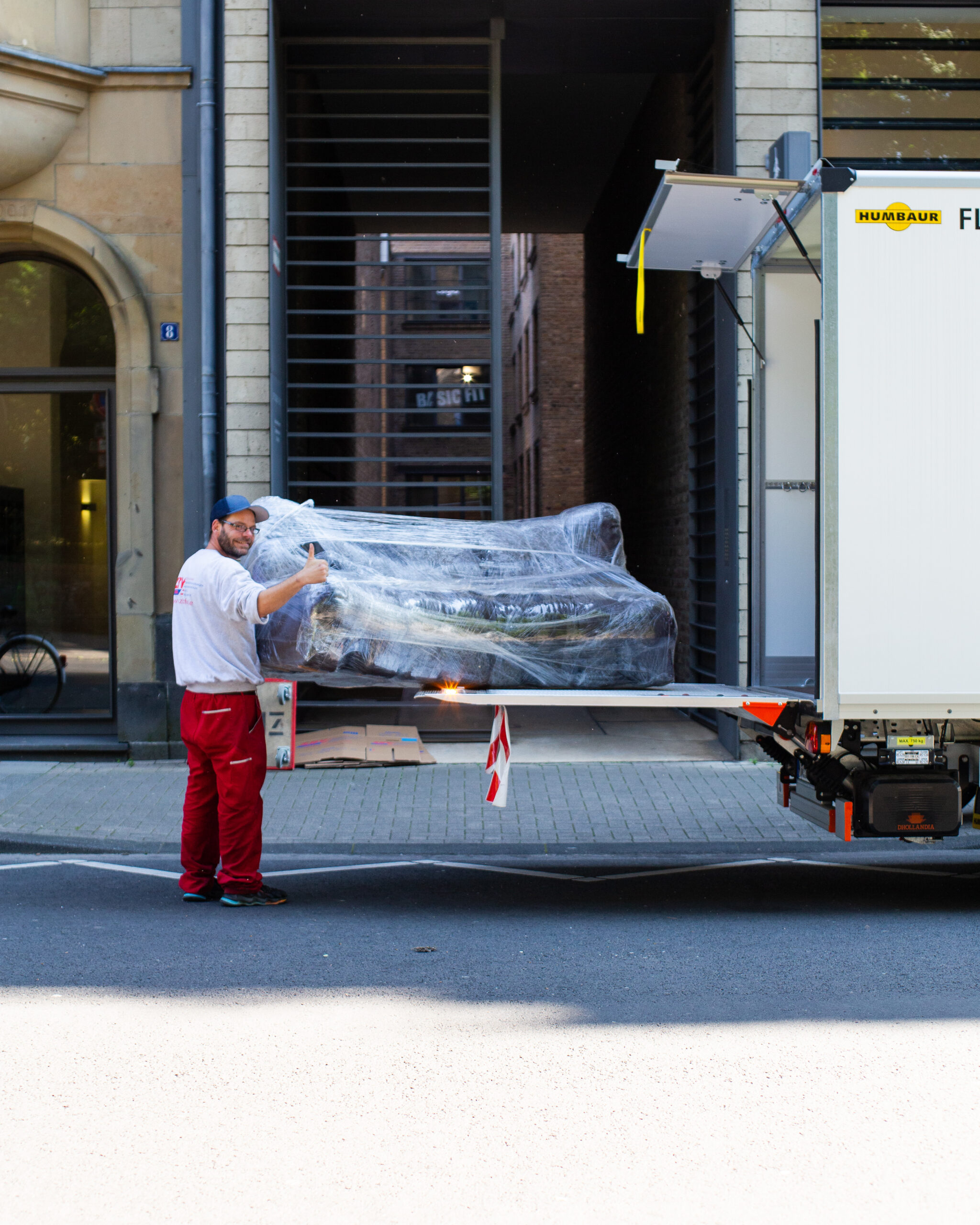 Ein Mitarbeiter hält ein eingepacktes Sofa auf einer LKW Laderampe