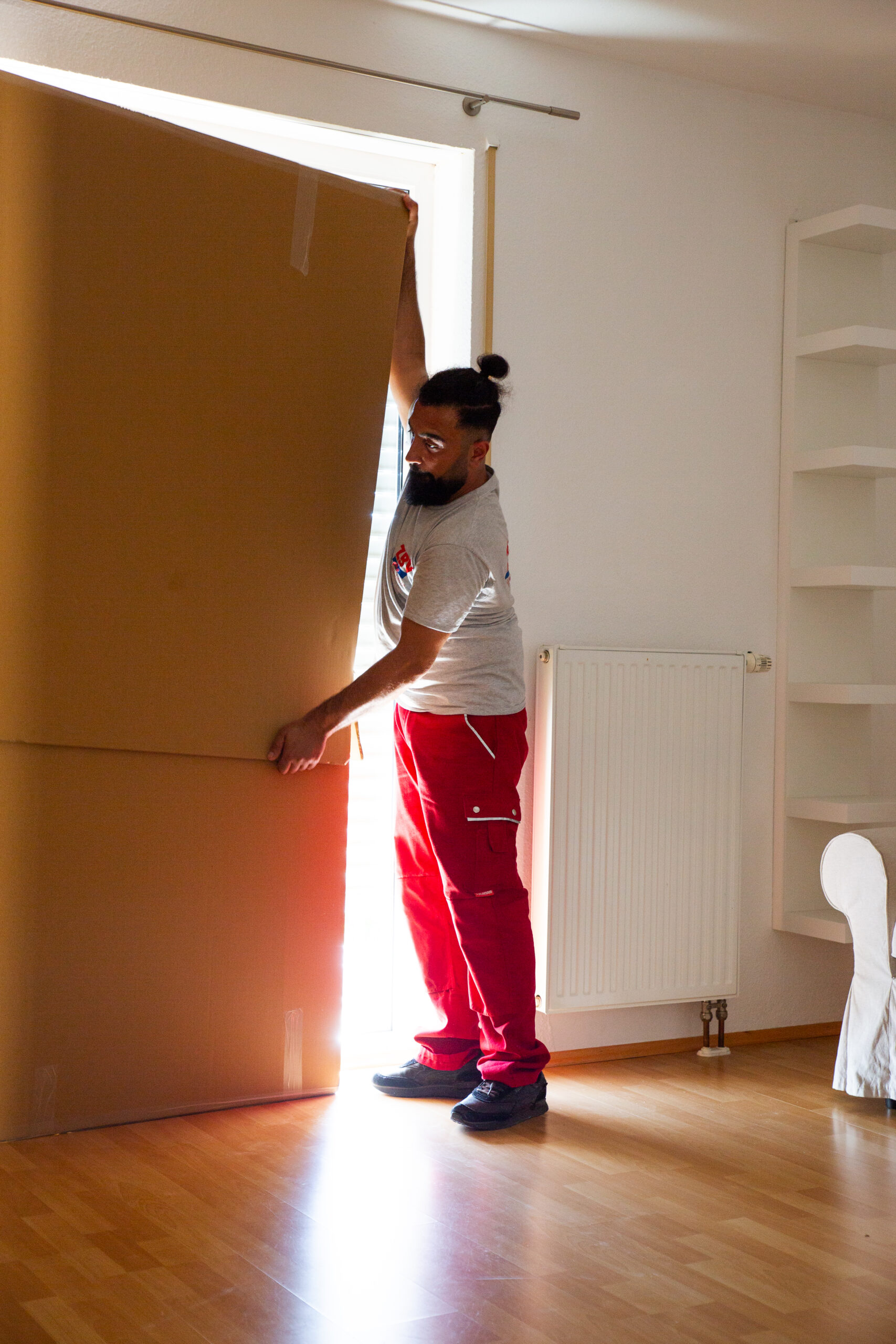 Mann trägt großen Karton in einen hellen Raum.