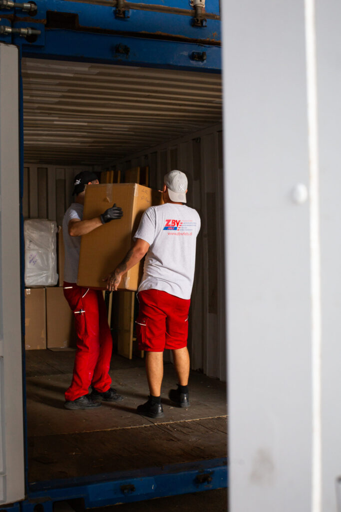 Zwei Männer laden Kartons in einen Container.