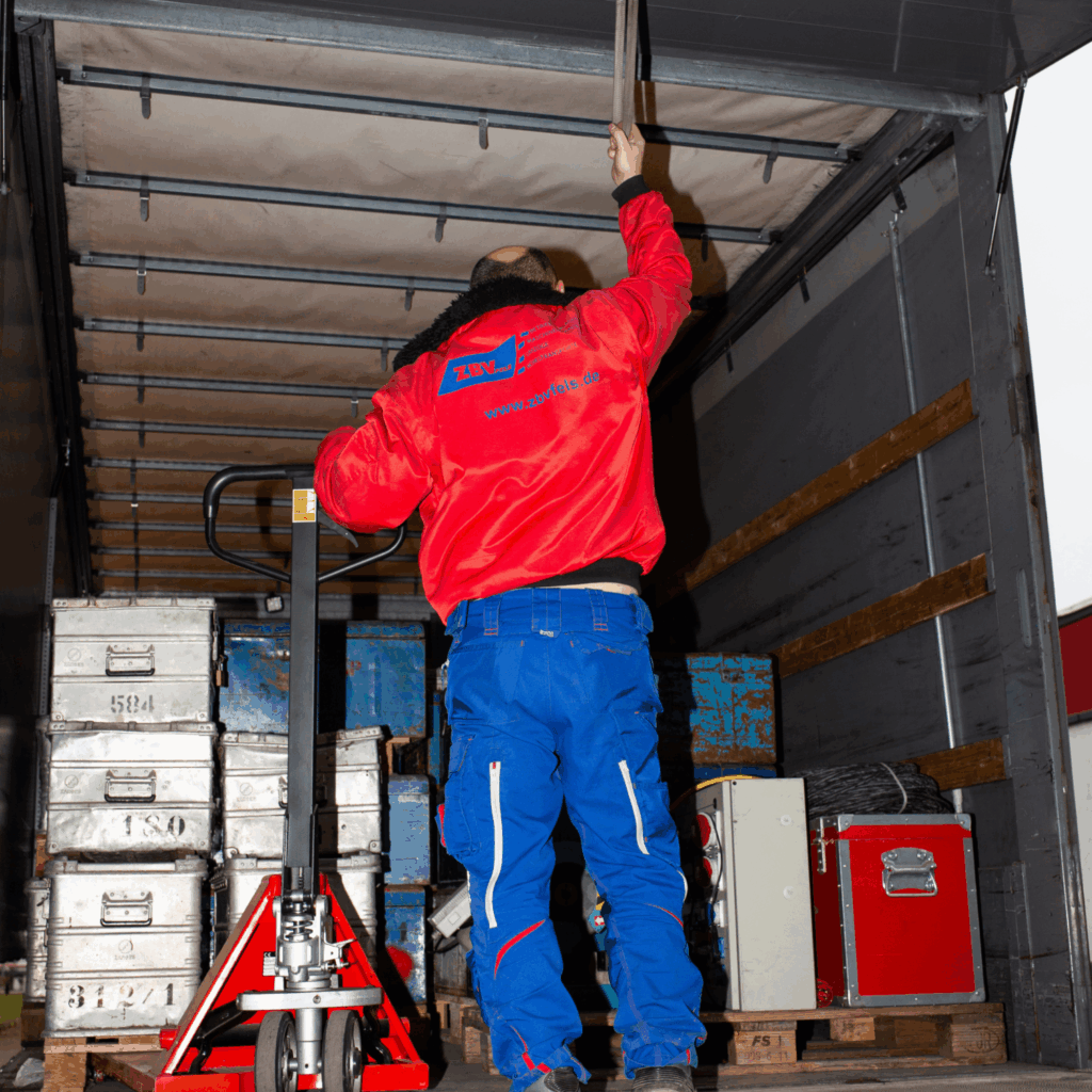 Reliable relocation services from ZBV Fels: An employee secures cargo in a truck using a pallet jack and stackable metal crates—ideal for moves, project logistics, and machinery relocation.