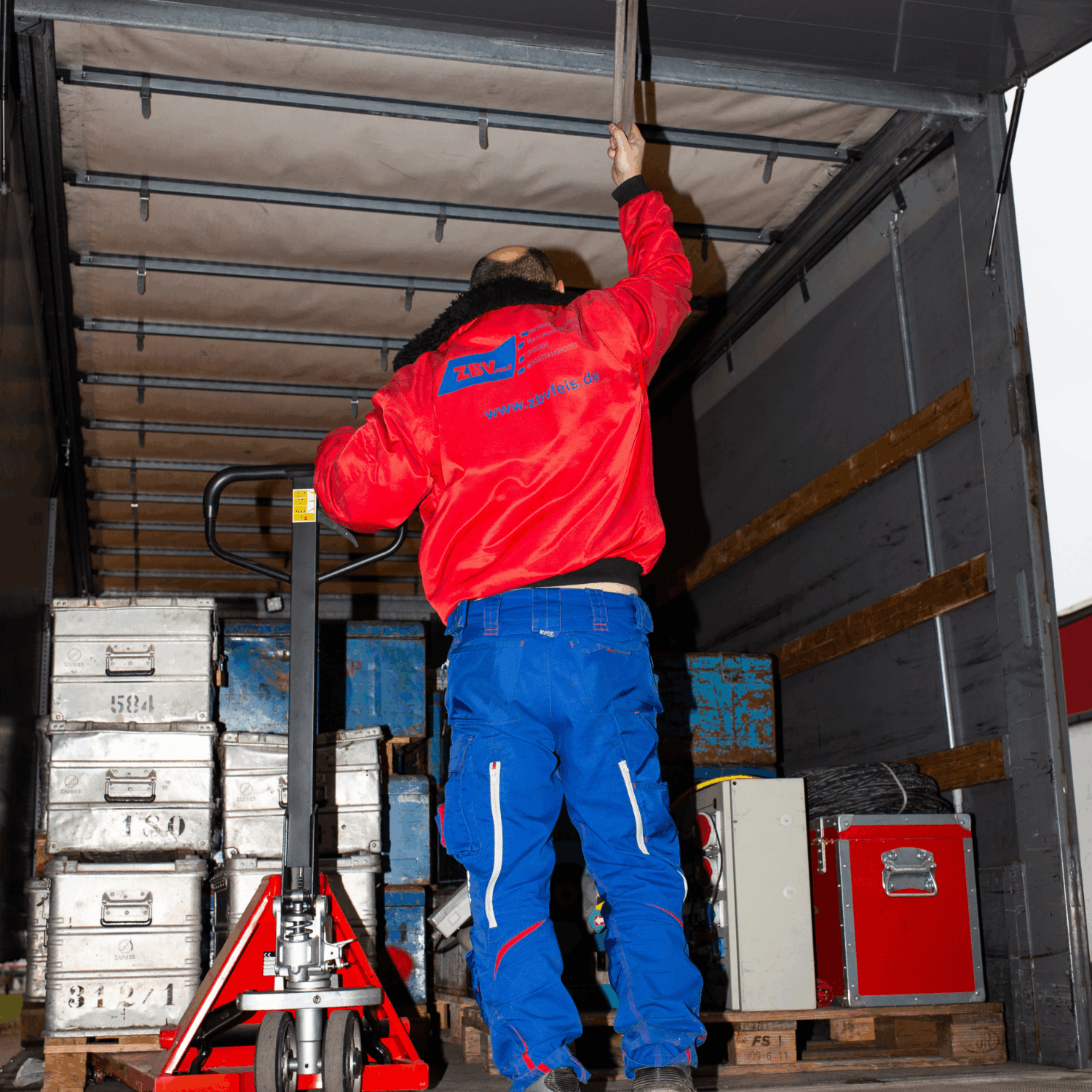 Zuverlässige Betriebsverlagerung von ZBV Fels: Mitarbeiter sichert Fracht im LKW mit Hubwagen und stapelbaren Metallkisten – ideal für Umzüge, Projektlogistik und Maschinenumzüge.