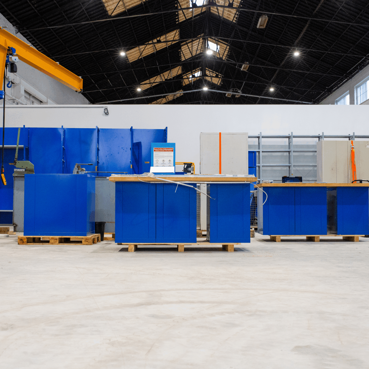 Industrielle Werkhalle mit mehreren blauen Werkbänken auf Paletten, sauberem Betonboden und hoher Hallendecke – vorbereiteter Arbeitsplatz für Maschinen- oder Montagearbeiten.