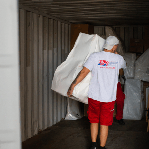 ZBV-Fels-Mitarbeiter trägt eine mit Schutzfolie verpackte Matratze in einen Lagercontainer – professionelle Einlagerung bei Umzügen oder temporärer Zwischenlagerung.
