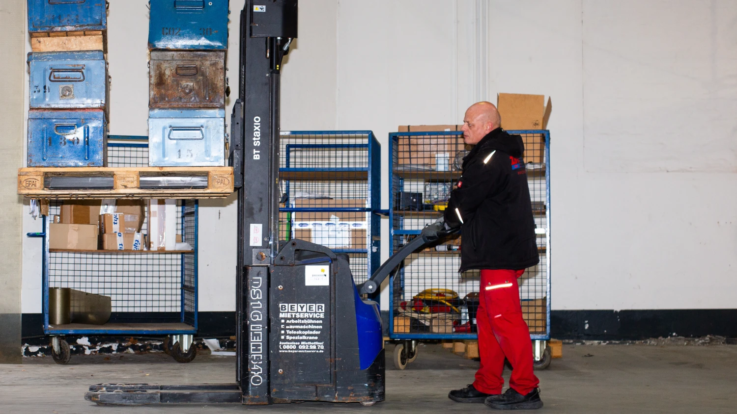 ZBV Fels Mitarbeiter beim Heben von Metallboxen mit Elektrohubwagen – sichere und effiziente Betriebsverlagerung für Industrie und Gewerbe