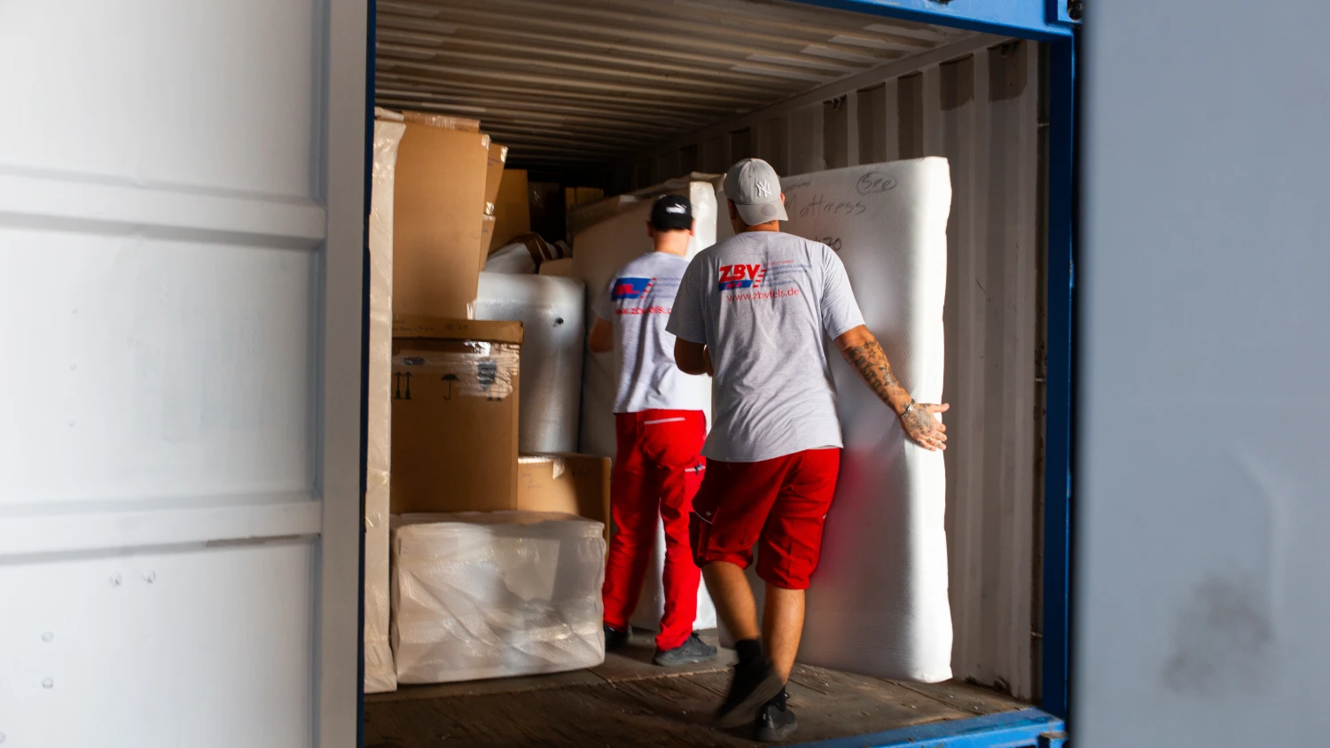 Zwei Mitarbeiter verladen gepolsterte Möbel und Kartons sorgfältig in einen Container – professioneller Einlagerungs- oder Umzugsservice durch ZBV Fels mit geschultem Personal.