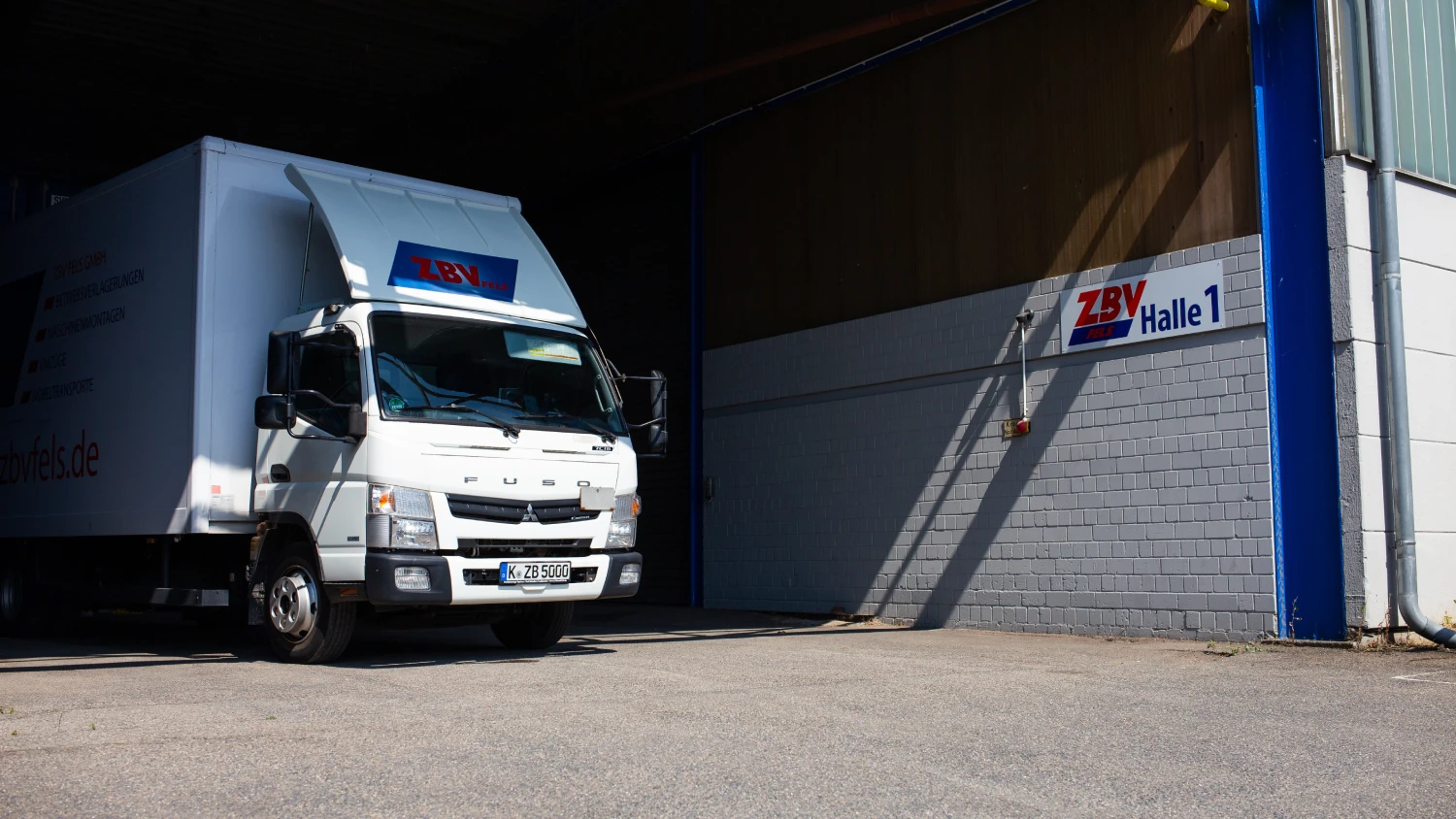 Zwei Mitarbeiter von ZBV Fels verladen professionell gepolsterte Möbel und Kartons in einen Container – sicherer Transport und strukturierte Einlagerung im Rahmen eines Selfstorage-Services.