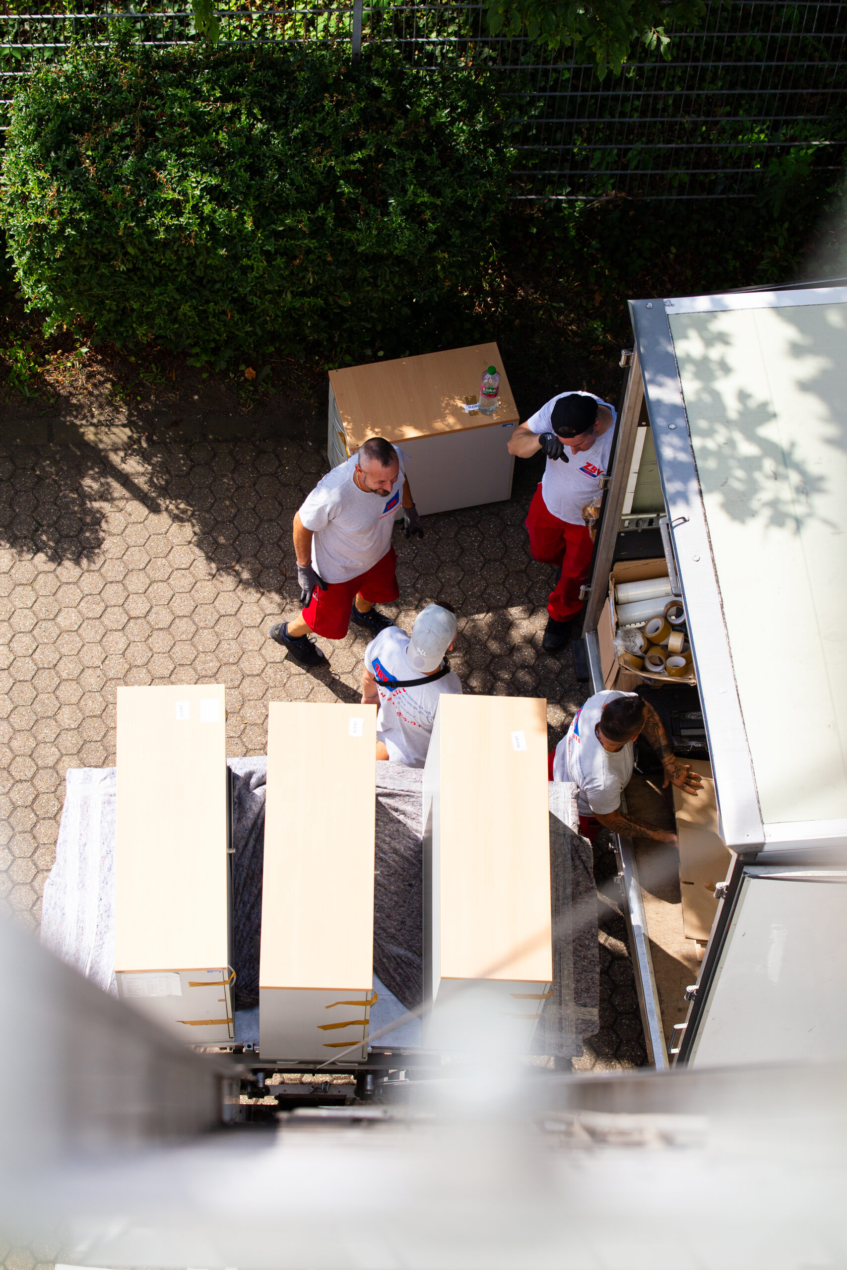 Aerial view of a professional moving team loading furniture into a van—a structured process with a focus on protective materials and teamwork.
