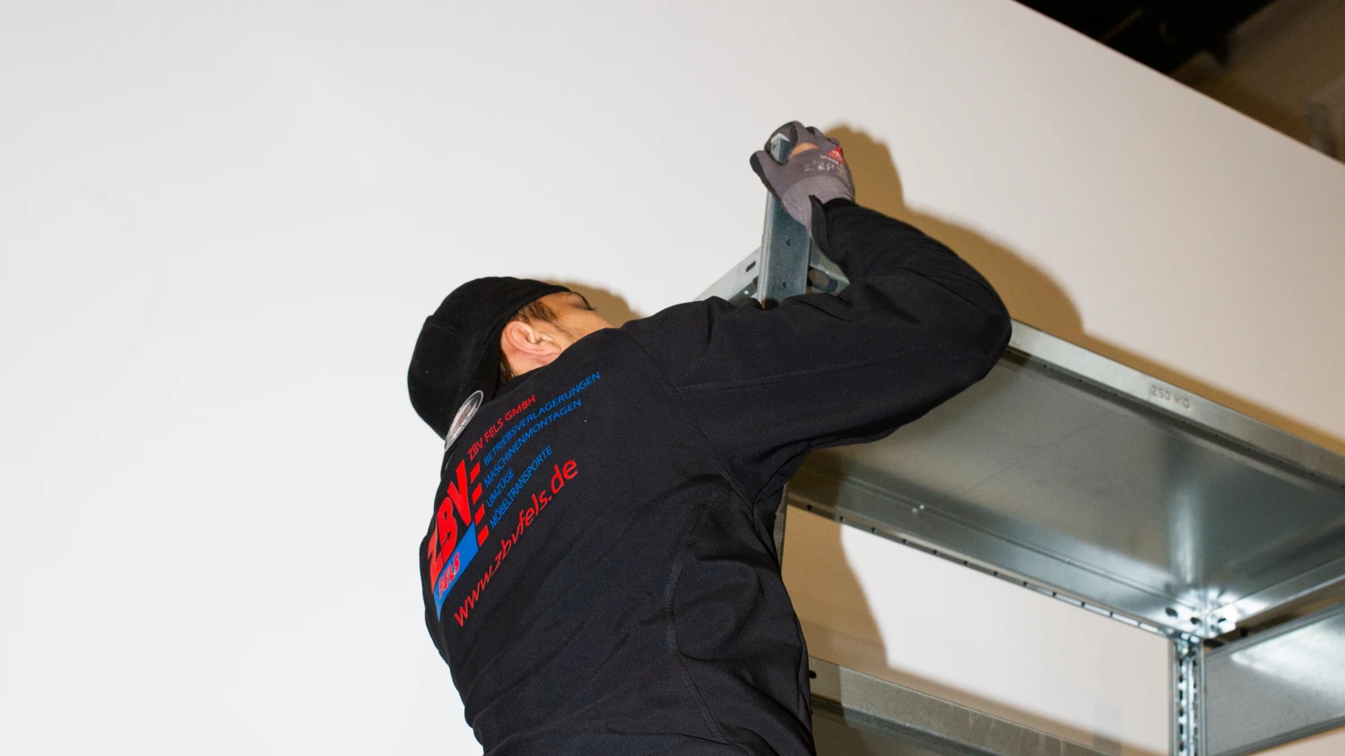 Fachkraft der ZBV Fels GmbH montiert ein stabiles Industrieregal an der Wand