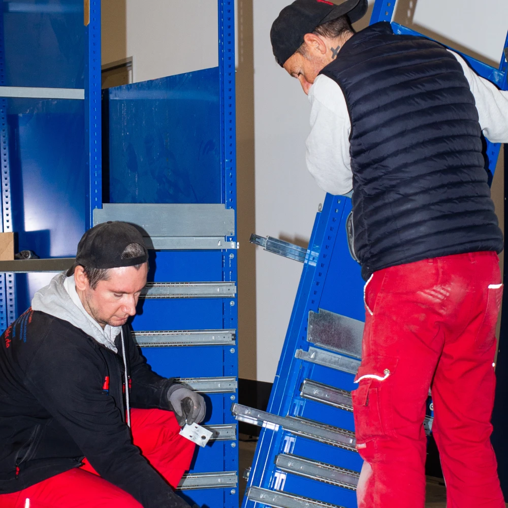 Zwei Monteure beim Aufbau eines blauen Regalsystems in einer Lagerhalle