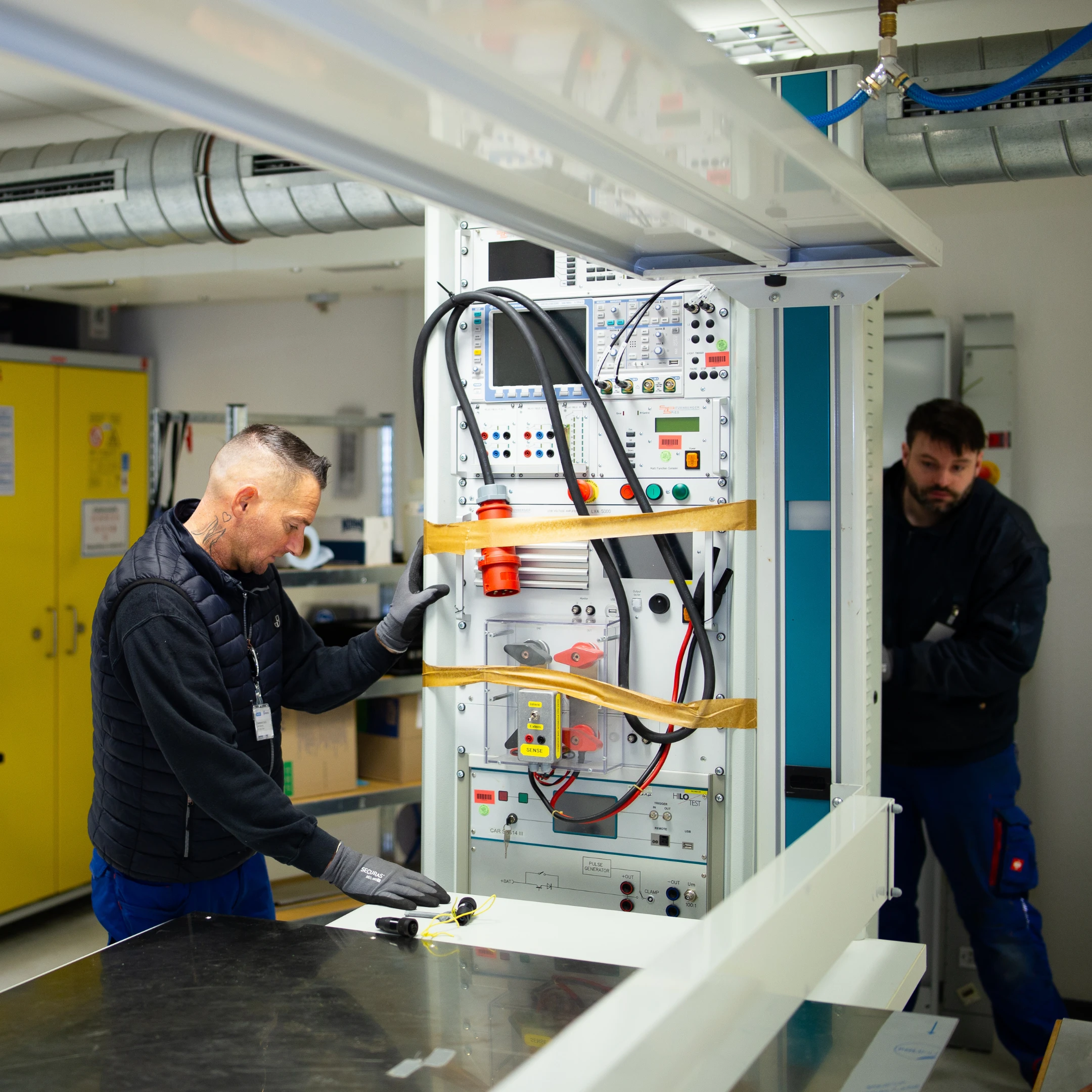 Zwei Männer arbeiten an einem technischen Gerät in einem Labor oder Werkstatt.