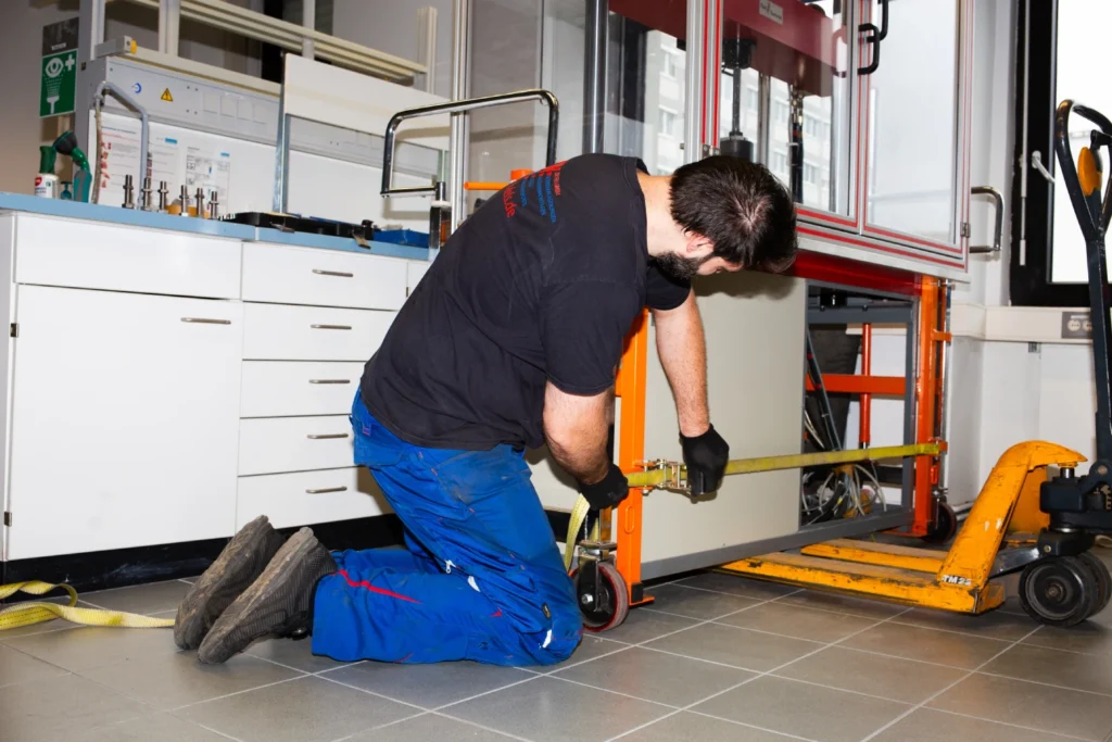A man is kneeling on the floor and operating a lifting device in a workshop.