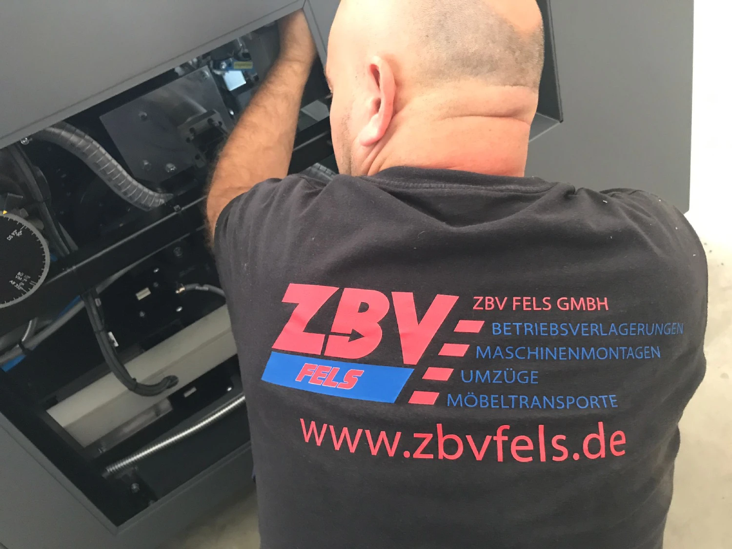 Mann mit schwarzem T-Shirt mit Firmenlogo arbeitet an einem Haushaltsgerät.