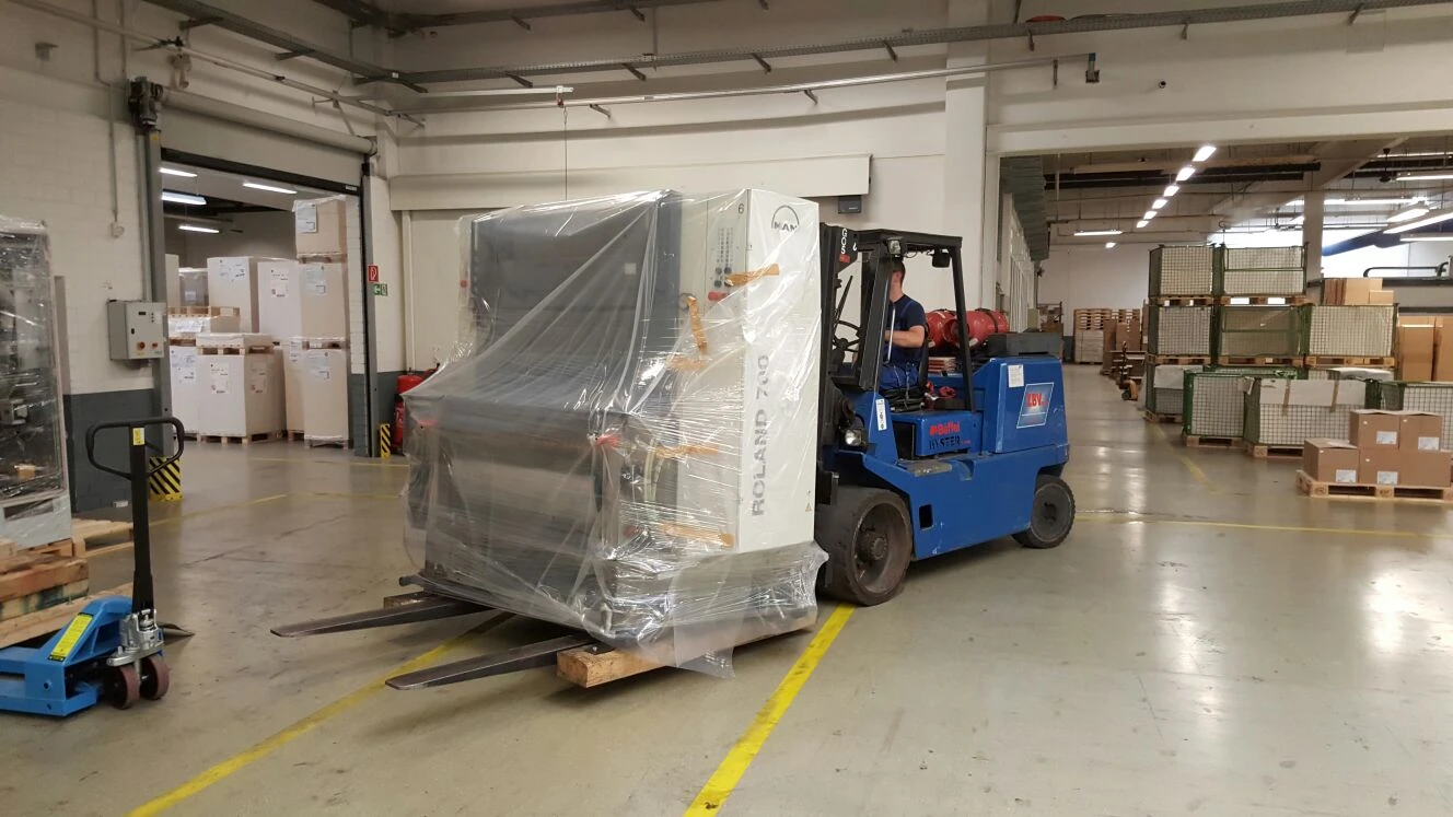 Gabelstapler transportiert verpackte Maschine in Lagerhalle.