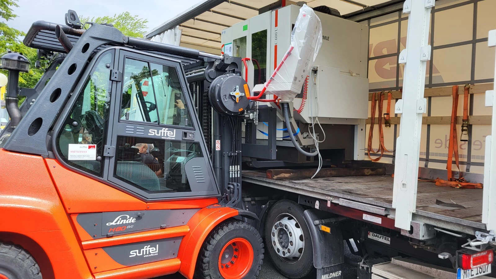 Gabelstapler lädt schwere Maschine auf LKW.