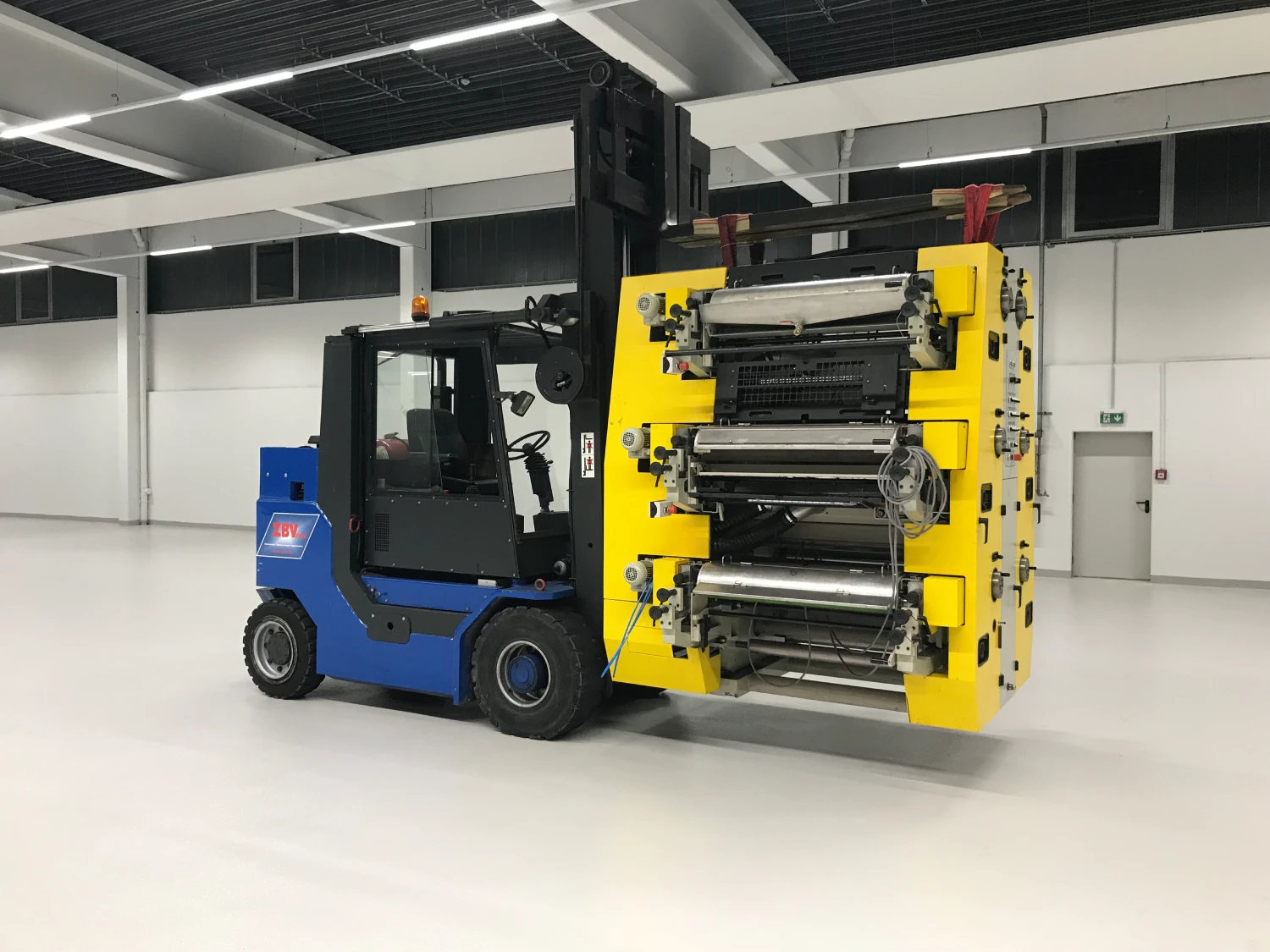 Gabelstapler hebt große gelbe Industriemaschine in leerer Halle.