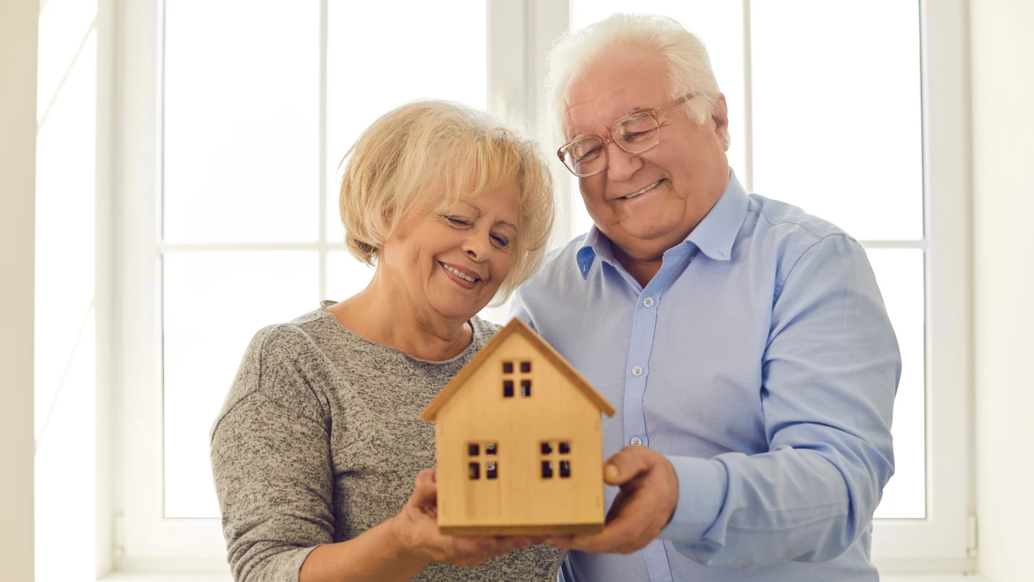 Älteres Paar hält gemeinsam ein kleines Modellhaus und lächelt.