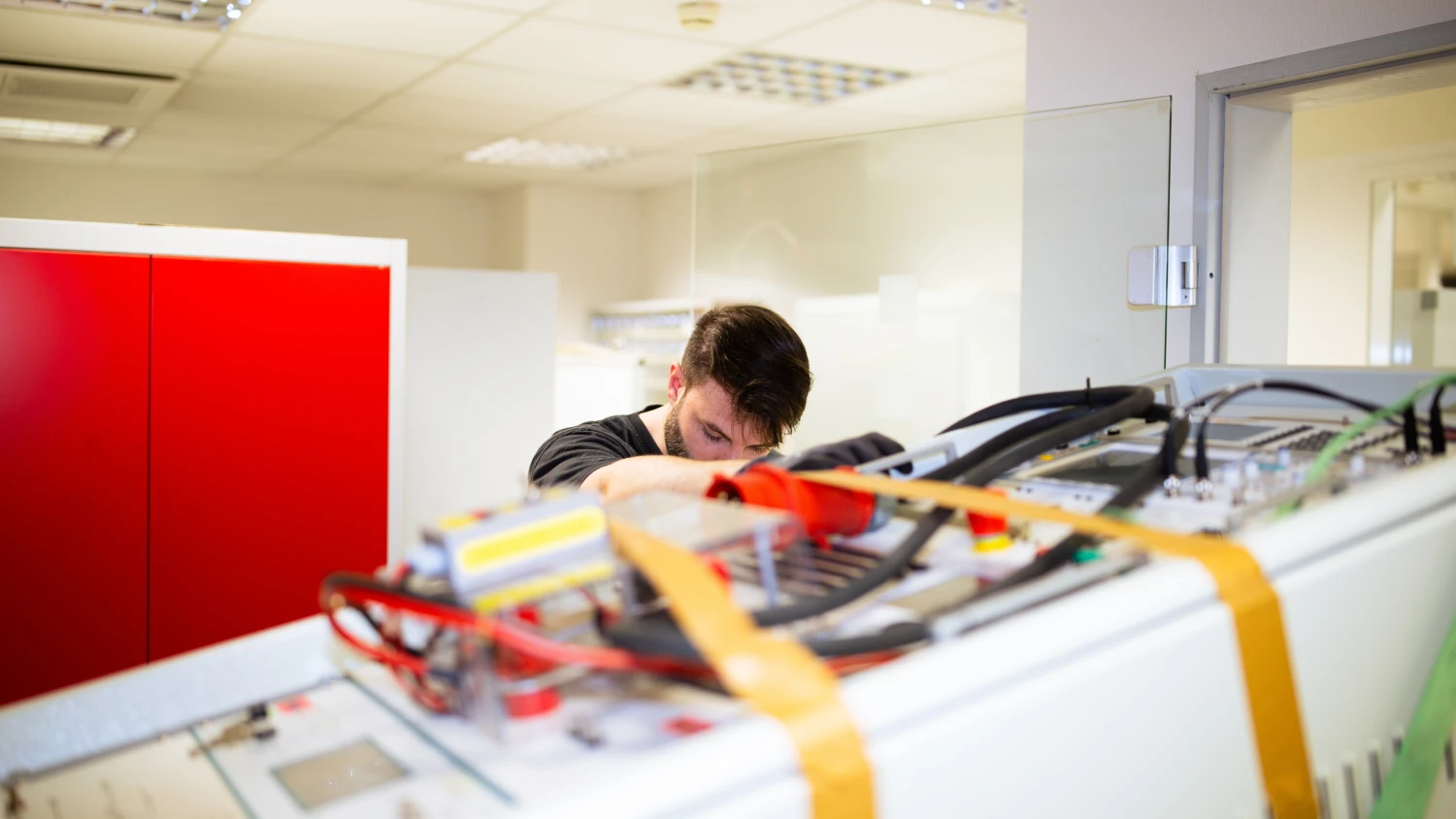 Techniker arbeitet an komplexem elektronischem Gerät mit Kabeln und Komponenten in einem Labor.
