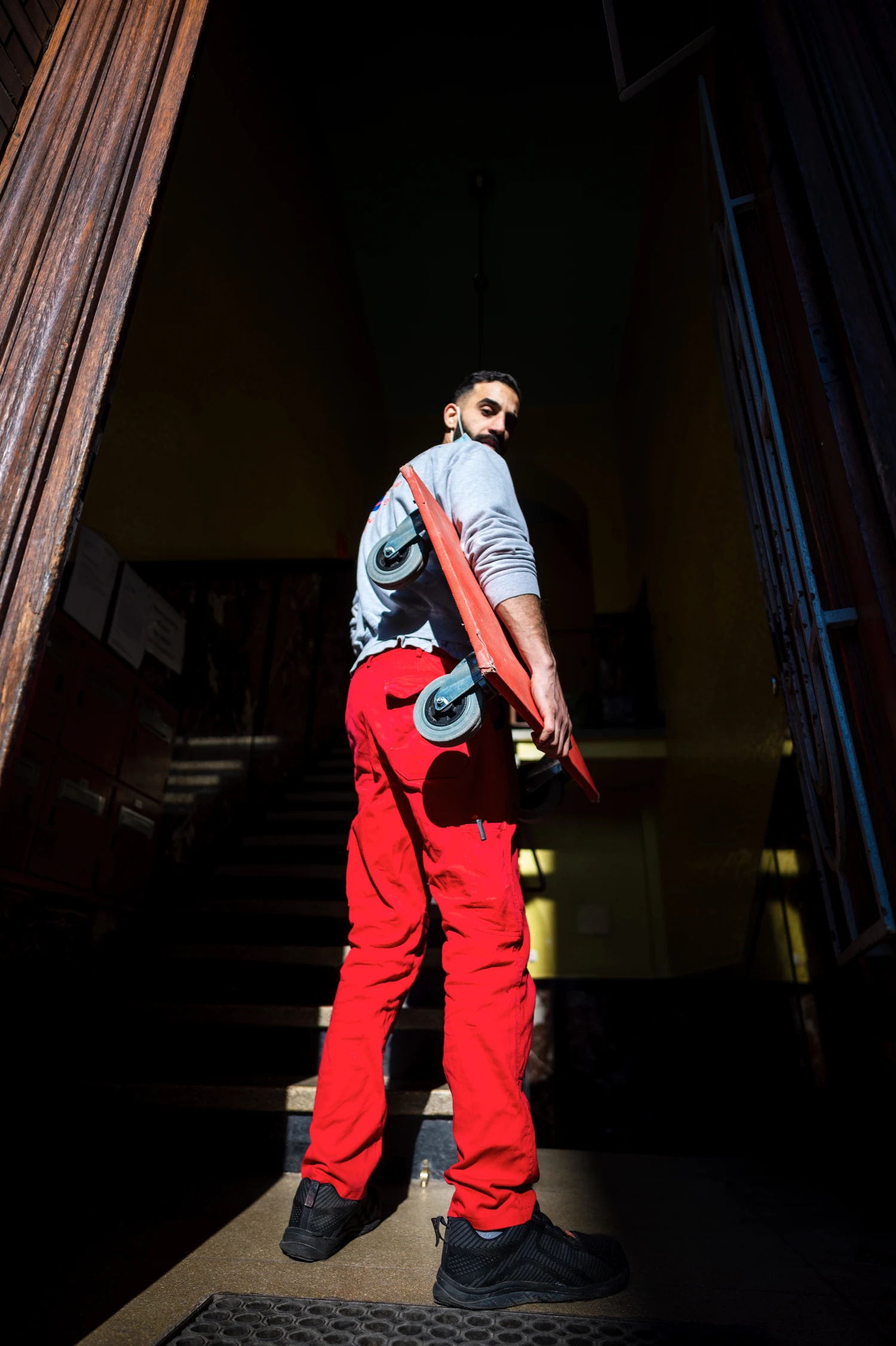 Mann mit roter Hose und Gitarre steht auf einer dunklen Treppe.