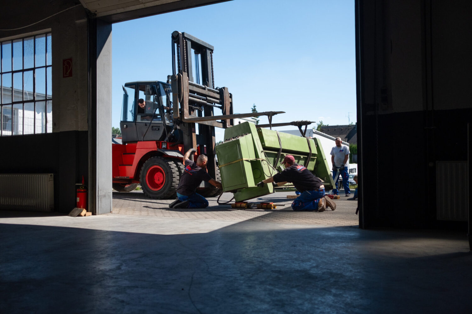 Gabelstapler transportiert grüne Industriemaschine, Mitarbeiter sichern Gerät