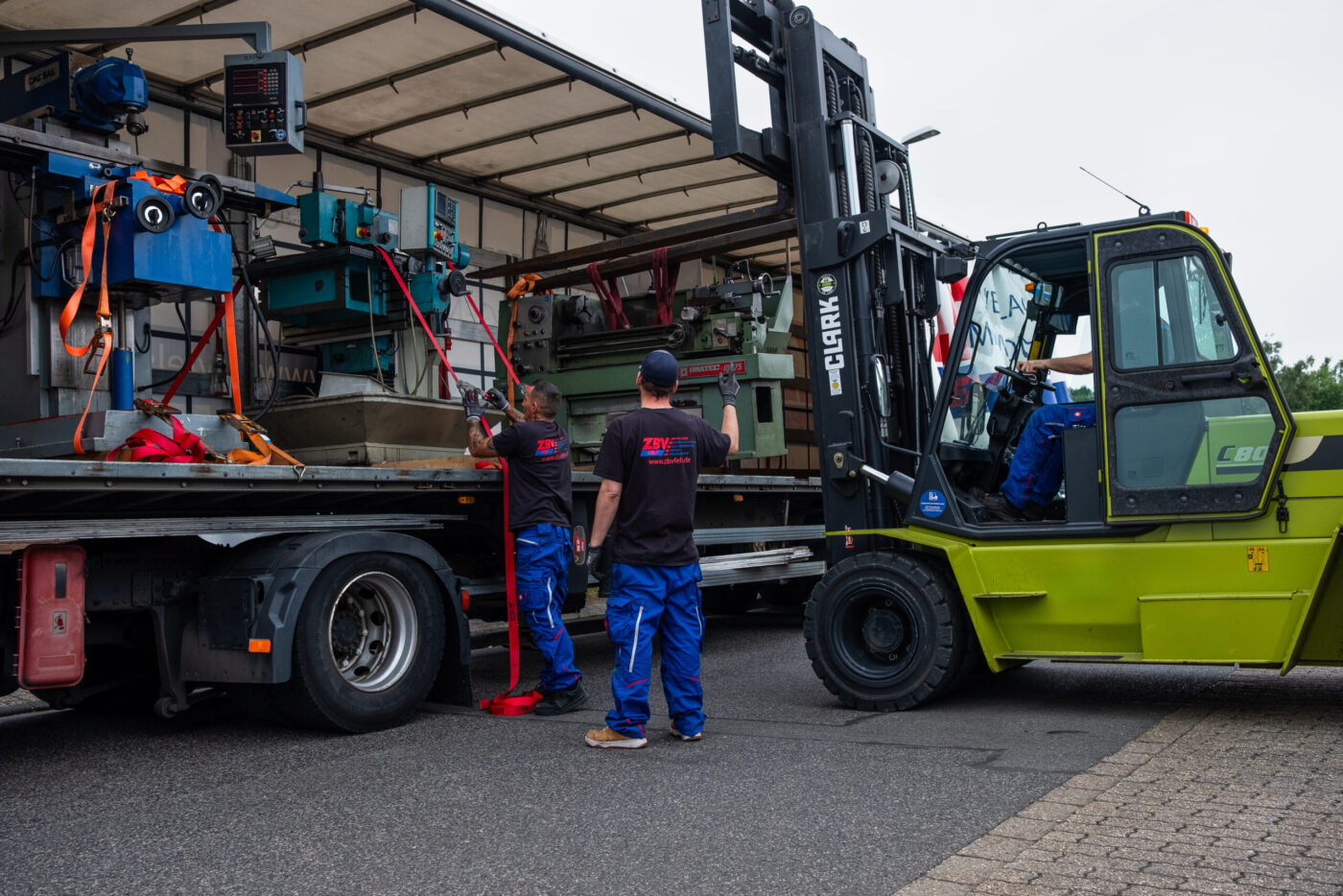 Team lädt Maschinen mit Gabelstapler in LKW ein und befestigt Spanngurte