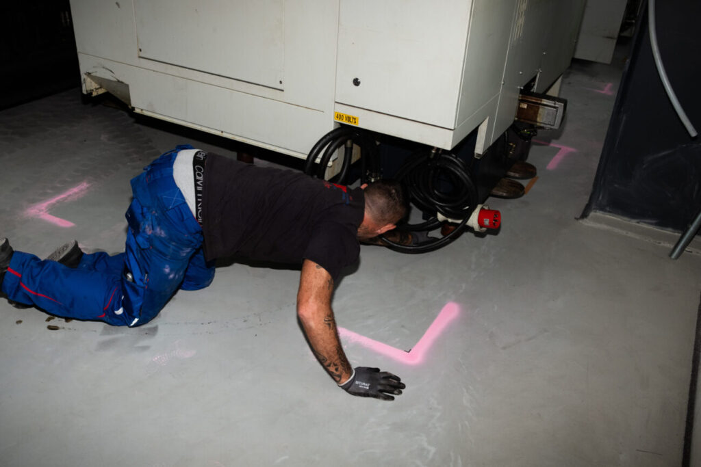 Worker inspects wiring under an industrial machine in a factory