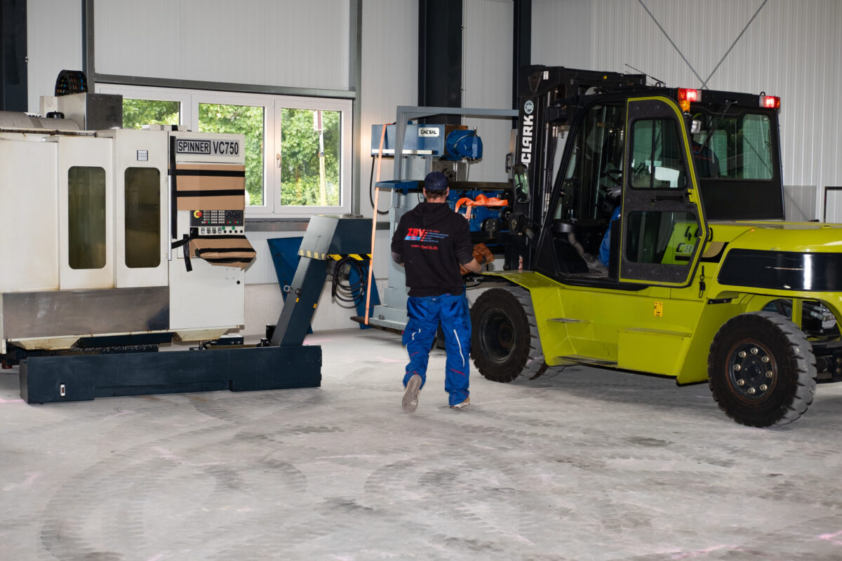 Mitarbeiter in Halle mit Gabelstapler und Industriemaschine