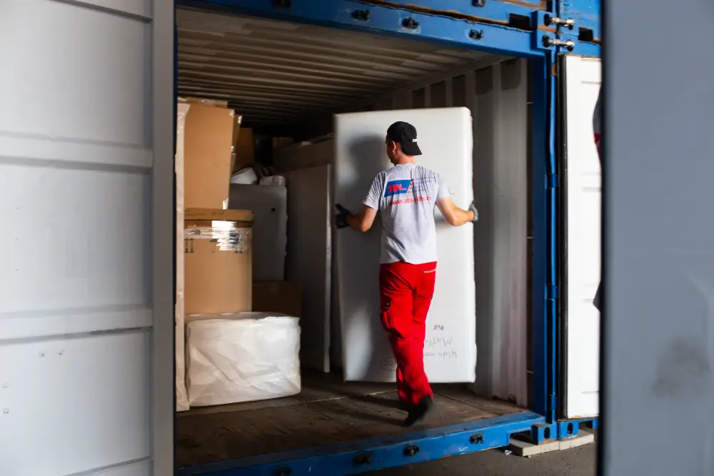 Mann trägt großen Karton in einen Container voller Pakete.