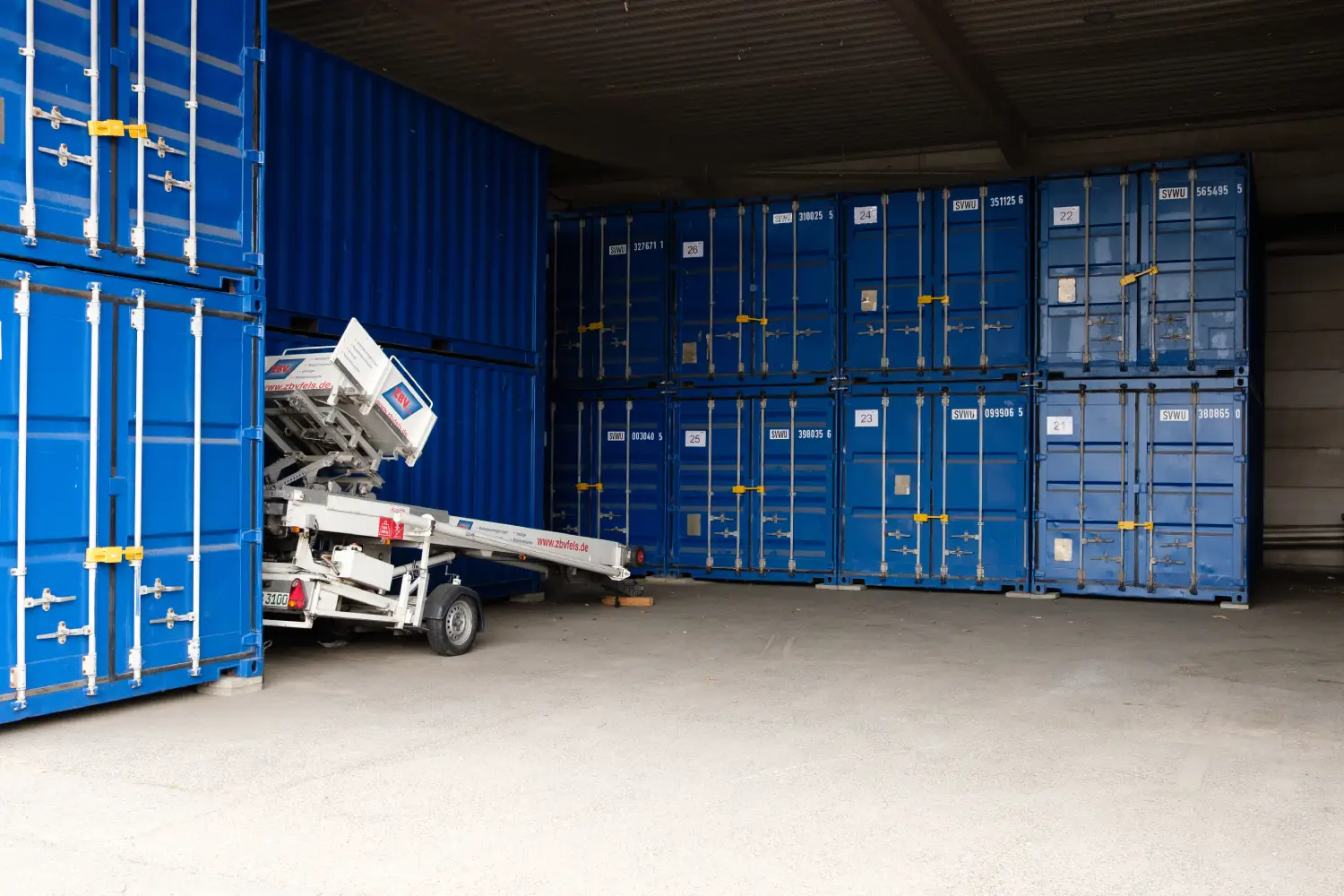 Lagerhalle mit gestapelten blauen Containern und Förderband.