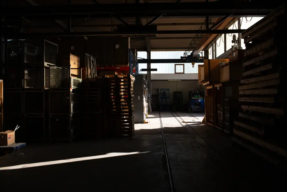 Dunkles Lagerhaus mit gestapelten Paletten und Lichtstrahlen, die durch Fenster fallen.