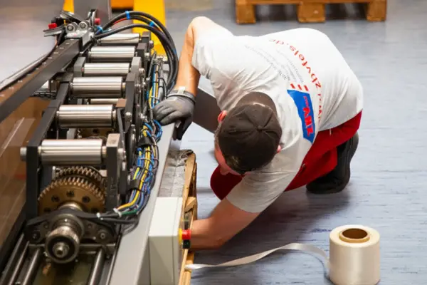 Mann in Arbeitskleidung überprüft eine Maschine in einer Werkstatt.