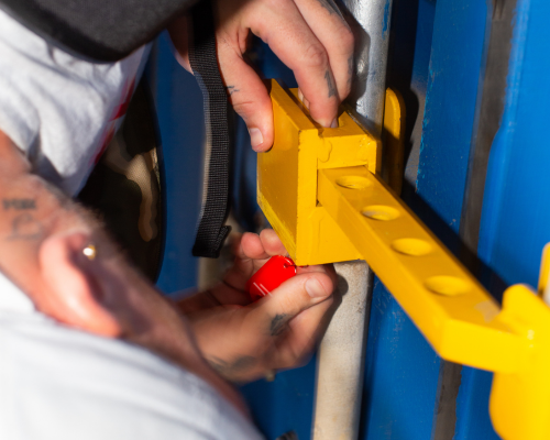 Person befestigt ein gelbes Sicherheitsverschlussgerät an einem blauen Schrankgriff.